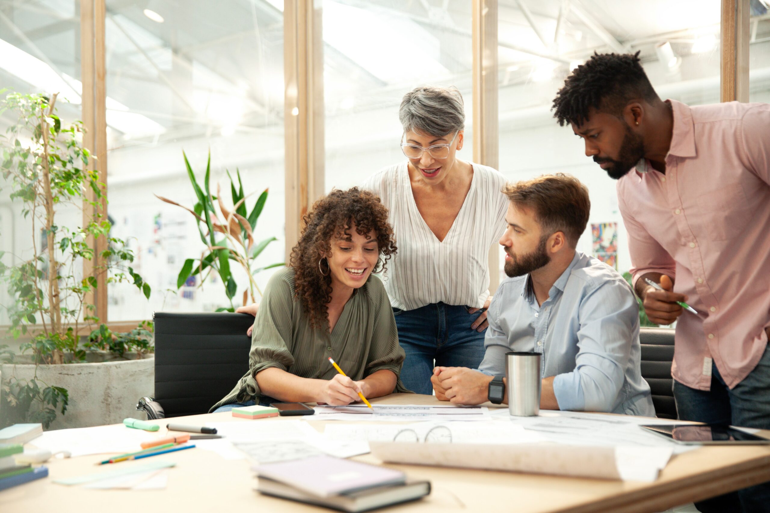 Wide view portrait of an older businesswoman talking to coworkers during a meeting, planning for retirement means working to maintain social connections like these.